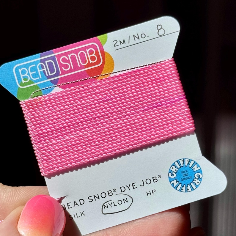 May include: A spool of bright pink nylon beading thread. The label reads "BEAD SNOB" and "DYE JOB". The thread is 2 meters long, size 8. The label also includes the Griffin logo, indicating it was made in Germany since 1866.
