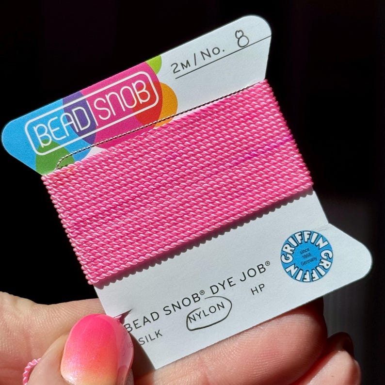 May include: A spool of bright pink nylon thread labeled "BEAD SNOB DYE JOB" and "SILK". The label also includes the text "2M/No. 8" and the Griffin logo. The thread is tightly wound and appears ready for use in jewelry making or crafts.