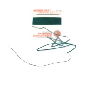 May include: A close-up of a spool of green thread with a label that reads "Natural Silk for stringing pearls and beads".
