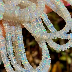May include: A strand of white opal beads with iridescent flashes of color. The beads are rectangular and have a slightly rounded shape.