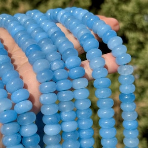 May include: A strand of light blue gemstone beads. The beads are round and smooth, and they have a slightly translucent appearance.
