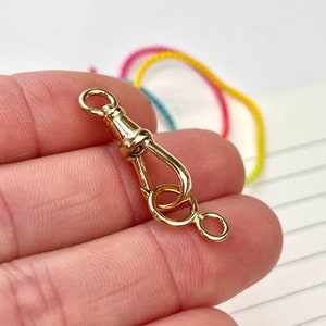 May include: Gold-toned metal clasp with a hook and a ring. The clasp is designed to attach to a chain or cord.