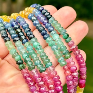 May include: A multi-strand necklace of faceted gemstone beads. The beads are arranged in a rainbow pattern, starting with yellow, then blue, green, and finally pink. The beads are all approximately the same size and shape.