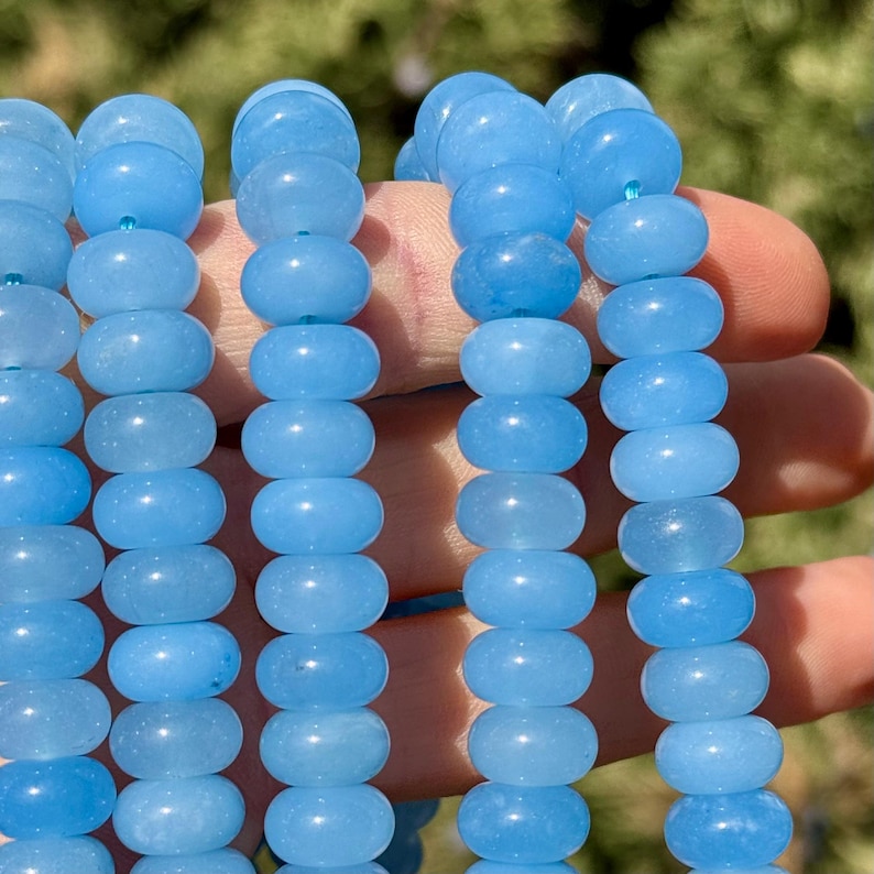 May include: A strand of light blue gemstone beads. The beads are round and smooth, and they have a slightly translucent appearance. The beads are strung on a clear elastic cord.