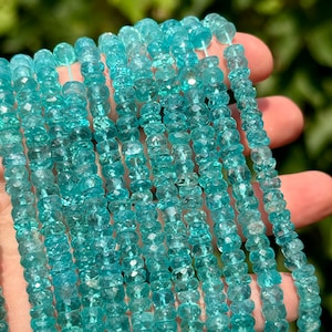 May include: Strands of faceted, light blue gemstones. The beads are strung together, creating a shimmering effect. The gemstones have a slightly irregular shape, adding to their unique appeal. The background is blurred, highlighting the beads.