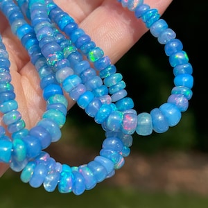 May include: A strand of blue opal beads with iridescent flashes of colour. The beads are round and have a smooth, polished finish.