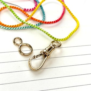 May include: A rainbow colored cord with a gold clasp and a gold ring. The cord is made of twisted yarn.