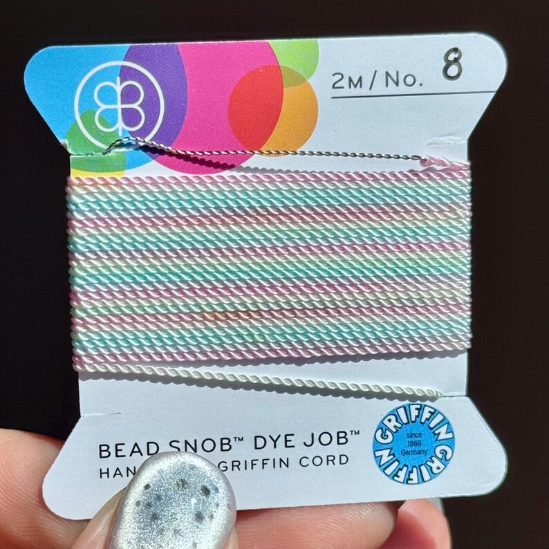 Peut inclure: Une bobine de cordon Griffin Bead Snob Dye Job. Le cordon est un m&eacute;lange de couleurs pastel, dont le rose, le vert et le blanc. L'&eacute;tiquette porte le texte "BEAD SNOB DYE JOB" et "GRIFFIN CORD". Le haut de l'&eacute;tiquette pr&eacute;sente un design color&eacute; et le num&eacute;ro 8.