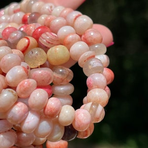 May include: A close-up of a strand of pink, white, and yellow agate beads. The beads are smooth and polished, and they have a natural, organic look.