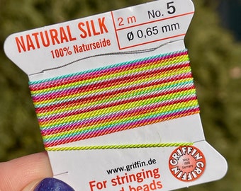 Peut inclure: Une bobine de 2 mètres de fil de soie naturelle, 100% Naturseide, d'un diamètre de 0,65 mm. Le fil est arc-en-ciel et est étiqueté "NATURAL SILK 2 m No. 5 Ø 0,65 mm 100% Naturseide" et "Pour enfiler des perles et des perles".
