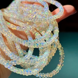 May include: A strand of small, translucent, round beads with an iridescent finish that reflects flashes of blue, green, and yellow light. The beads are strung together in a continuous loop, creating a shimmering, multi-layered circular pattern.