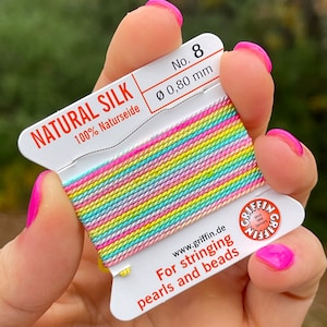 May include: A spool of rainbow colored natural silk thread for stringing pearls and beads. The spool is labeled "NATURAL SILK 100% Naturseide" and "No. 8 Ø 0,80 mm".
