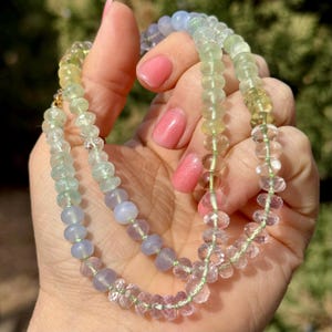 May include: A multi-colored gemstone necklace with beads in shades of blue, green, and pink. The necklace is made with faceted and round beads.