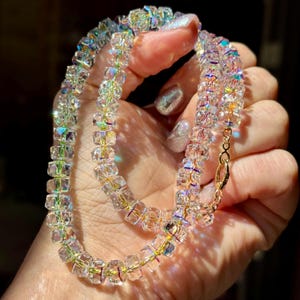 May include: A necklace composed of clear, faceted, iridescent crystal beads strung on a thin gold-toned wire. The beads exhibit a multi-colored light reflection, and the necklace is secured with a small gold-toned metal lobster claw clasp.