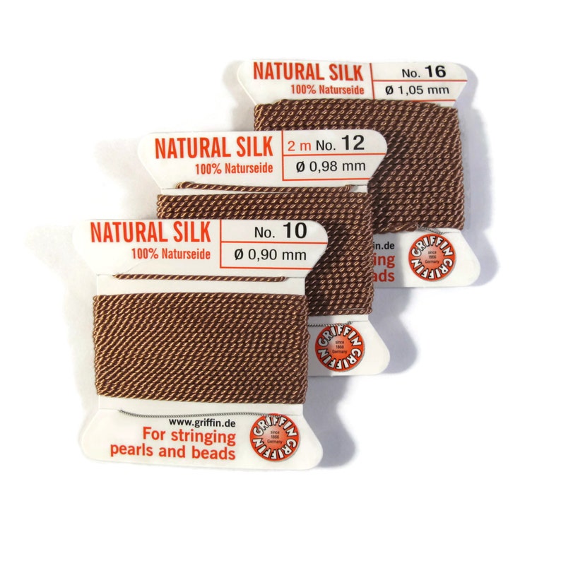 May include: Three spools of brown natural silk thread for stringing pearls and beads. The spools are labeled "Natural Silk 100% Naturseide" with the size and number of the thread. The spools are labeled "No. 16 &Oslash; 1,05 mm", "2 m No. 12 &Oslash; 0,98 mm", and "No. 10 &Oslash; 0,90 mm".