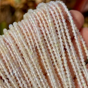 Puede incluir: Una hebra de cuentas de vidrio facetadas blancas iridiscentes. Las cuentas son pequeñas y redondas, y tienen un brillo sutil.