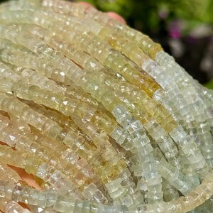 Pu&ograve; includere: Primo piano di fili di perline di pietre preziose sfaccettate, giallo-verde chiaro. Le perline sono piccole, rettangolari e infilate insieme, creando un effetto strutturato e scintillante. La sfumatura di colore passa dal giallo pallido al verde traslucido.