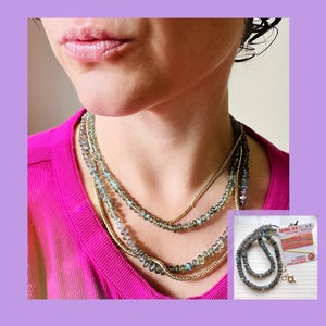 May include: A layered necklace with multiple strands of iridescent blue-green beads and a gold chain. The necklace is worn by a person with a pink shirt.