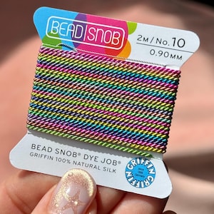 Puede incluir: Un carrete de cordón de seda 100% natural de la marca Bead Snob, tamaño n.º 10, 0,90 mm, 2 metros de largo. El cordón presenta un vibrante patrón de degradado de arcoíris multicolor con un brillo metálico, enrollado en una tarjeta blanca.