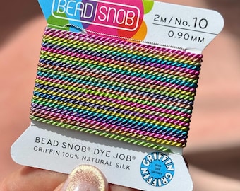Peut inclure: Une bobine de cordon en soie 100% naturelle de la marque Bead Snob, taille n° 10, 0,90 mm, 2 mètres de long. Le cordon présente un motif dégradé arc-en-ciel multicolore vibrant avec un éclat métallique, enroulé sur une carte blanche marquée.
