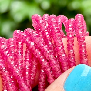 May include: A strand of pink faceted gemstone beads. The beads are small and round, and they are strung together on a clear thread. The beads are arranged in a spiral pattern.