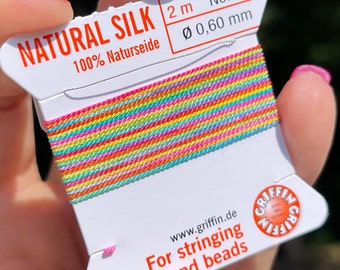 Peut inclure: Une bobine de fil de soie naturelle de couleur arc-en-ciel pour enfiler des perles et des perles. La bobine est étiquetée "NATURAL SILK 100% Naturseide 2m No. 4 0,60 mm" et "www.griffin.de For stringing pearls and beads".