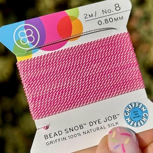 May include: A spool of pink beading thread labeled "Bead Snob™ Dye Job™ Griffin 100% Natural Silk" with the Griffin logo and "2m/ No. 8 0.80 mm" printed on the label.
