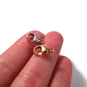 May include: Two lobster claw clasps, one silver and one gold, are shown on a finger.