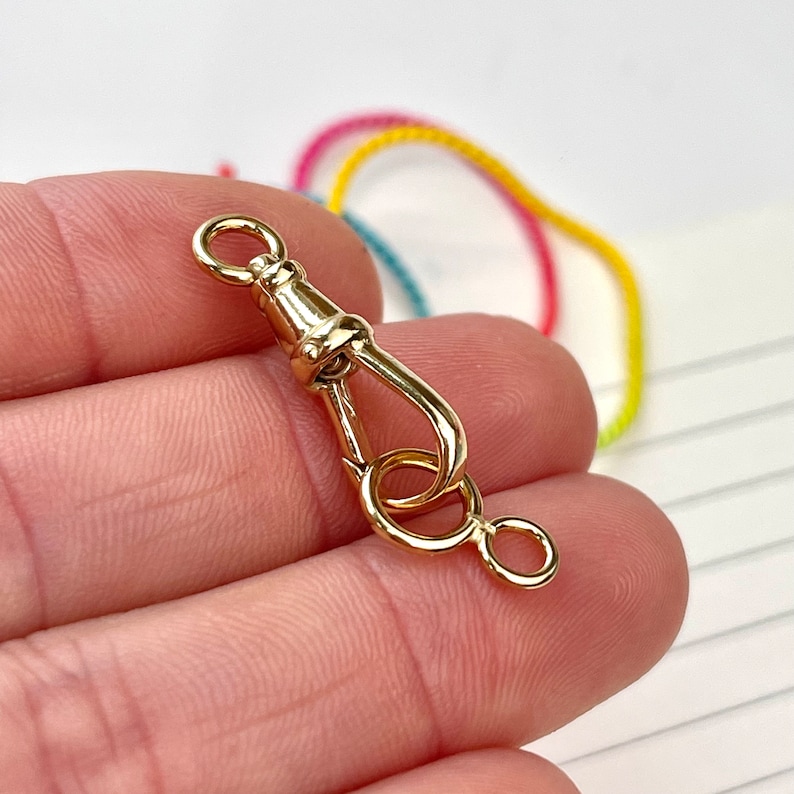 May include: Gold-toned metal clasp with a hook and a ring. The clasp is designed to attach to a chain or strap.