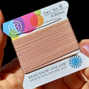 May include: A spool of pink beading thread labeled "Bead Snob Dye Job Griffin 100% Natural Silk" with the size "2m/ No. 8 0.80 mm" printed on the label.
