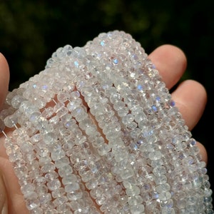 May include: A strand of white moonstone beads with iridescent shimmer. The beads are faceted and have a square shape. The beads are strung on a clear thread.