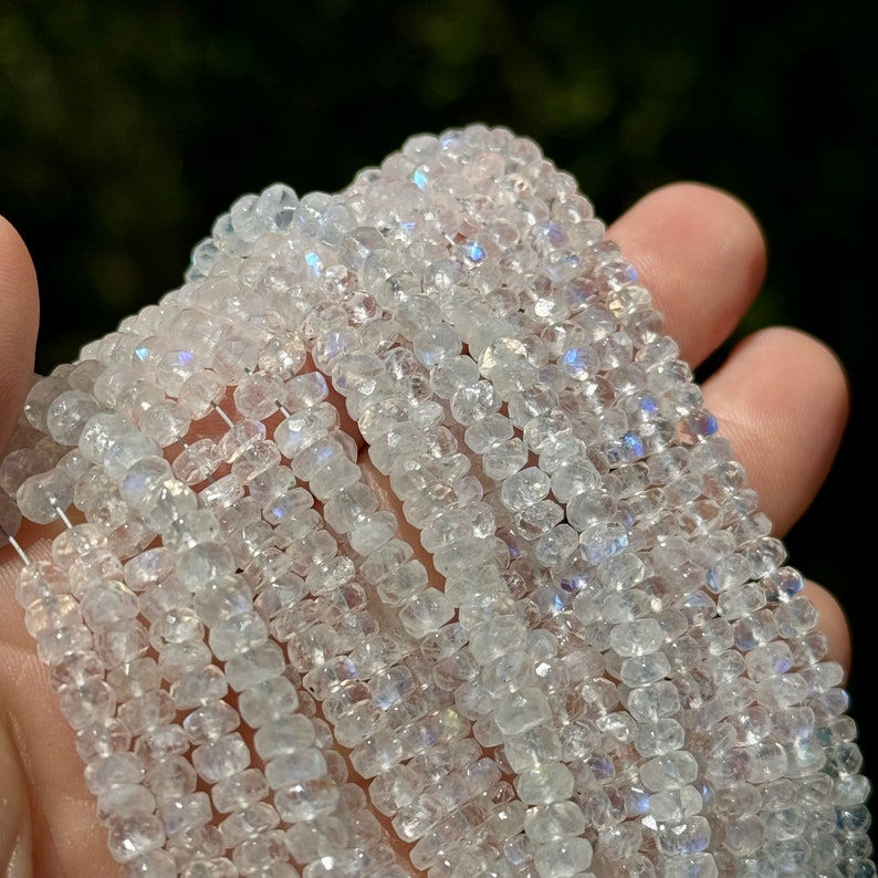 May include: A strand of white moonstone beads with iridescent shimmer. The beads are faceted and have a square shape. The beads are strung on a clear thread.
