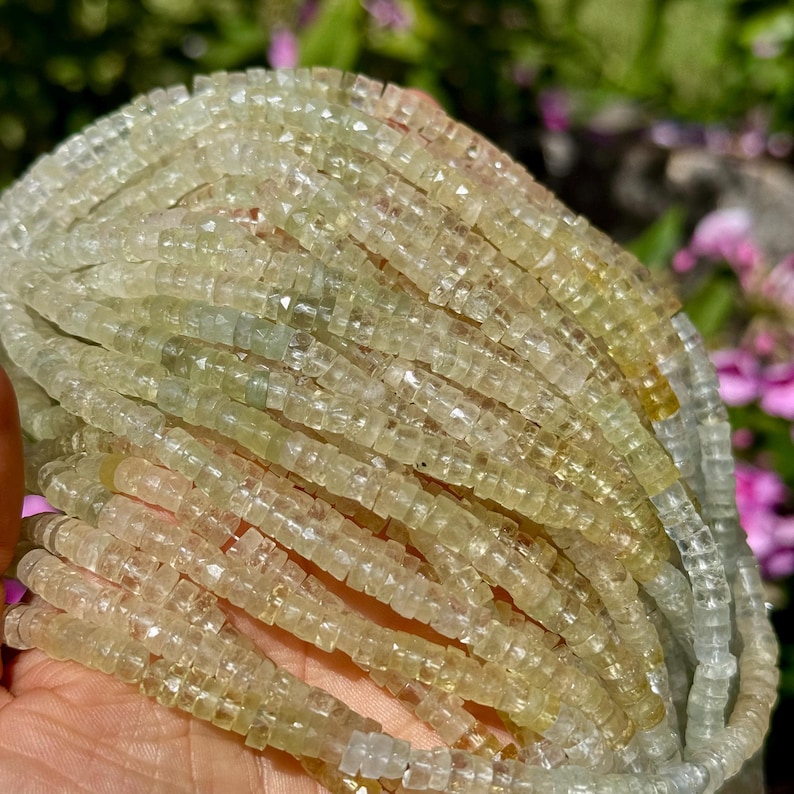 Pu&ograve; includere: Fili di perline di pietre preziose giallo-verde chiaro. Le perline sono piccole, tagliate a forma quadrata e infilate insieme, creando un effetto strutturato e stratificato. Le perline hanno una qualit&agrave; traslucida, con variazioni di colore.