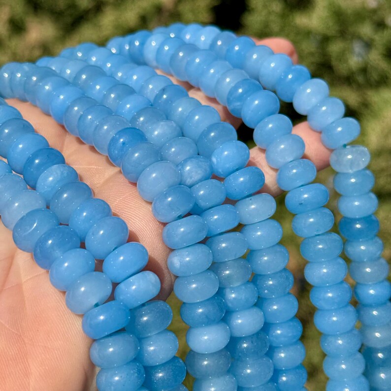 May include: A strand of light blue gemstone beads. The beads are round and smooth, and they have a slightly translucent appearance.