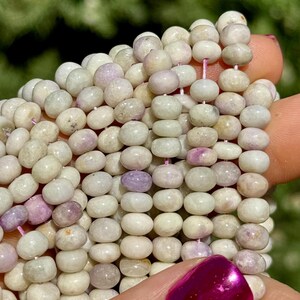 May include: A strand of white and lavender gemstone beads. The beads are round and have a slightly irregular shape. They are strung on a thin, pink thread.