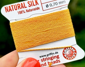 May include: A spool of natural silk thread, 100% Naturseide, in a bright yellow color. The spool is labeled "No. 6 Ø 0,70 mm" and "www.griffin.de stringing and beads".