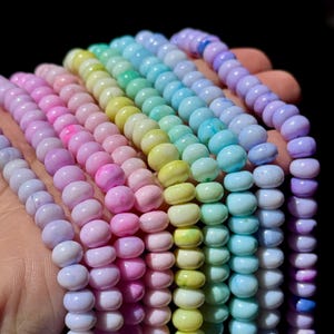 May include: Multiple strands of smooth, round beads in a gradient of pastel colors including lavender, light pink, pale yellow, mint green, and sky blue. The beads have a glossy finish and are arranged in parallel rows, showcasing a soft color palette.