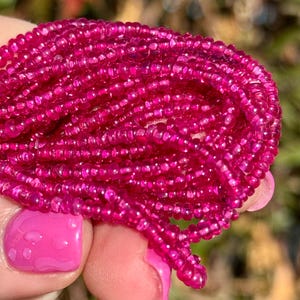 Może przedstawiać: Zbliżenie na sznur żywych różowych koralików z kamieni szlachetnych. Koraliki są małe, okrągłe i mają wypolerowane, błyszczące wykończenie. Kolor jest głęboki, nasycony różowy, z niewielką zmiennością odcienia. Koraliki są nawleczone.