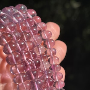 Puede incluir: Una hebra de cuentas de amatista púrpura, cada cuenta es lisa y redonda con un ligero brillo.