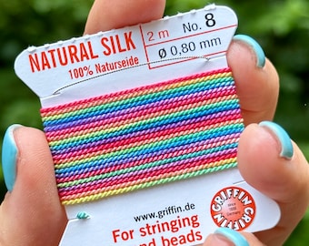 May include: Rainbow coloured natural silk thread for stringing pearls and beads. The spool is labelled "Natural Silk 2 m No. 8 Ø 0.80 mm 100% Naturseide" and "www.griffin.de For stringing pearls and beads".