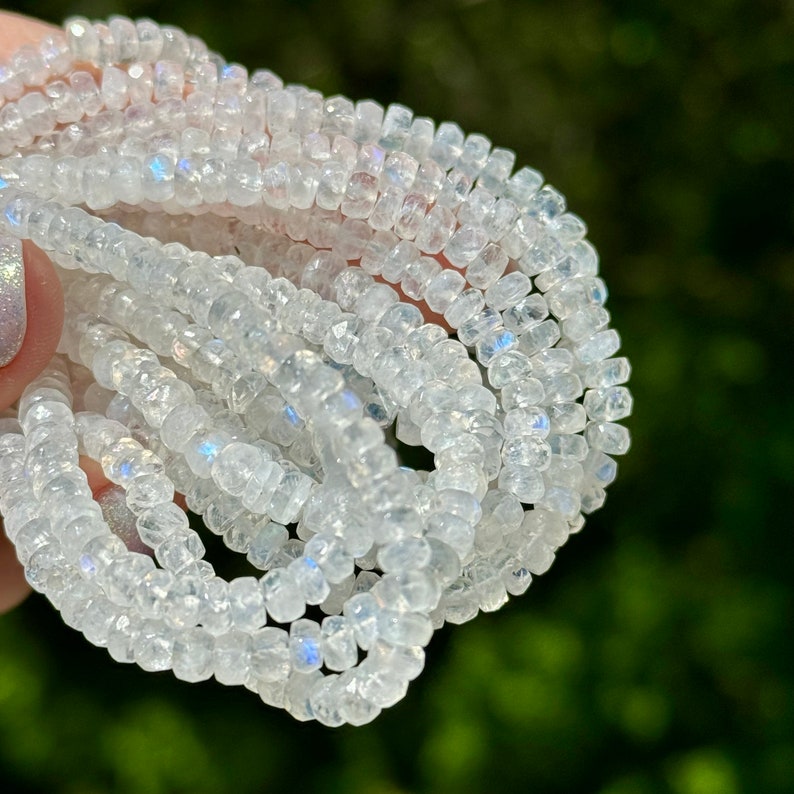 May include: A strand of white iridescent moonstone beads. The beads are faceted and have a slightly irregular shape. The beads are strung on a clear thread.