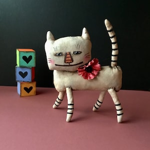 cat art fabric sculpture doll, sandy mastroni , grin, smile , a little creepy, fabric flower , white ,, standing  shelf doll,