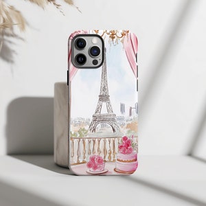 May include: A white iPhone case with a watercolor illustration of the Eiffel Tower, a pink curtain, and two pink cakes with pink roses on top. The case has a black border.