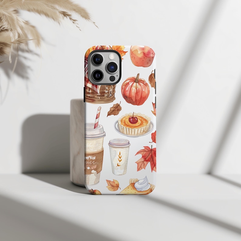May include: A white iPhone case with a fall-themed design. The design features a pumpkin, apple, pie, coffee cups, and fall leaves in shades of orange, brown, and red.