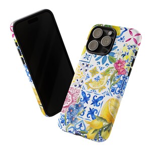 May include: A white iPhone case with a colorful pattern of blue, yellow, and pink tiles, lemons, and flowers. The case has a cutout for the camera lens.