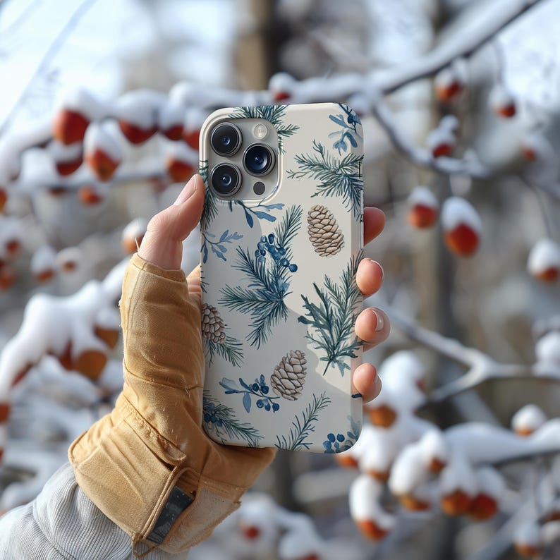 May include: A white phone case with a wintery design featuring pine branches, pine cones, and blue berries.