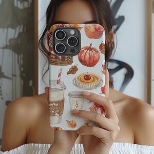 May include: White iPhone case with a fall-themed design featuring a pumpkin, pie, leaves, and a cup of pumpkin spice. The text "Pumpkin Spice" is visible on the cup.