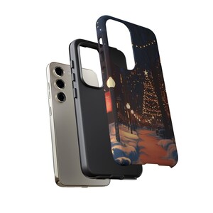 May include: A black phone case featuring a winter scene of a snowy street with a Christmas tree and fairy lights. The case is shown with a gold phone.