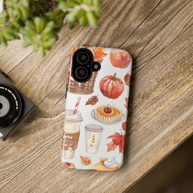 May include: A white phone case with a fall-themed design. The case features illustrations of pumpkins, apples, pies, coffee cups, and leaves in shades of orange, red, brown, and yellow.