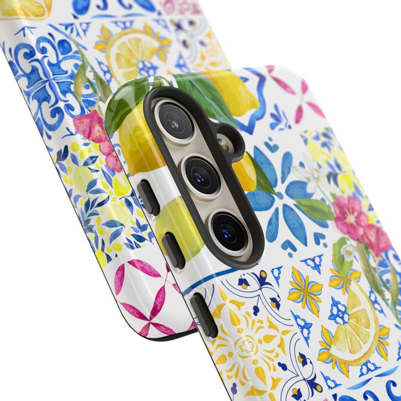 May include: A white phone case with a colorful pattern of lemons, flowers, and blue and white tiles. The case has a cutout for the camera lens.